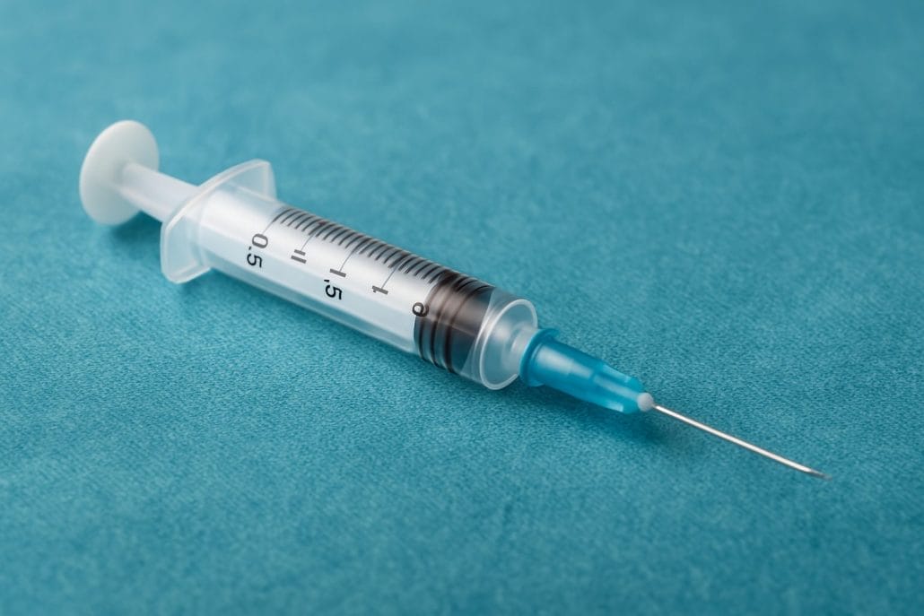 Jeringuilla estéril sobre campo quirúrgico azul, lista para uso médico en procedimientos articulares.